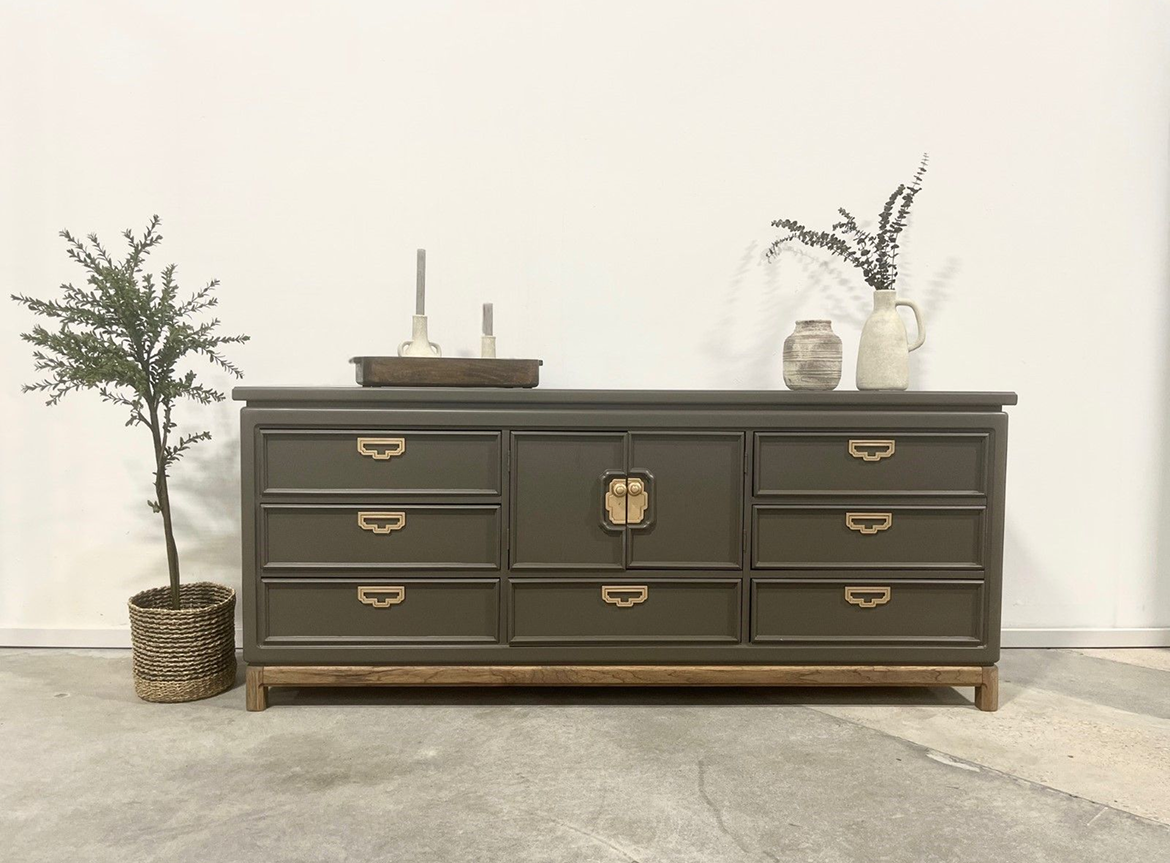 A dresser with many drawers and two plants in the middle